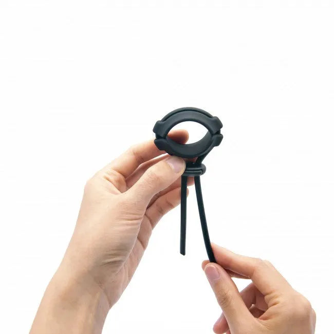 Anneau pénien ajustable noir en silicone avec fermeture coulissante, ergonomique et étanche, tenu par des mains.