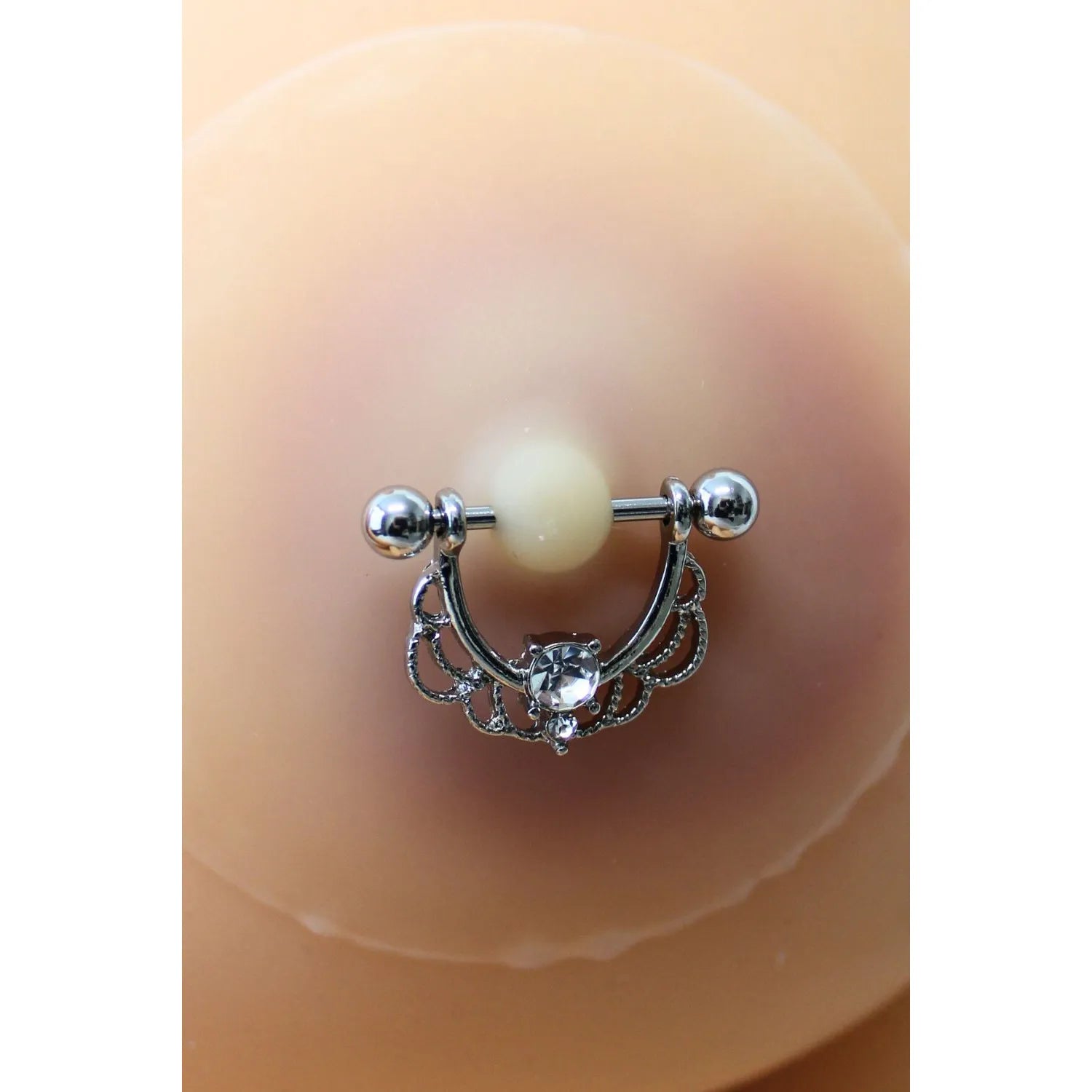 Cache-tétons silicone couleur chair avec piercing demi-anneau strass, design élégant pour peaux claires.