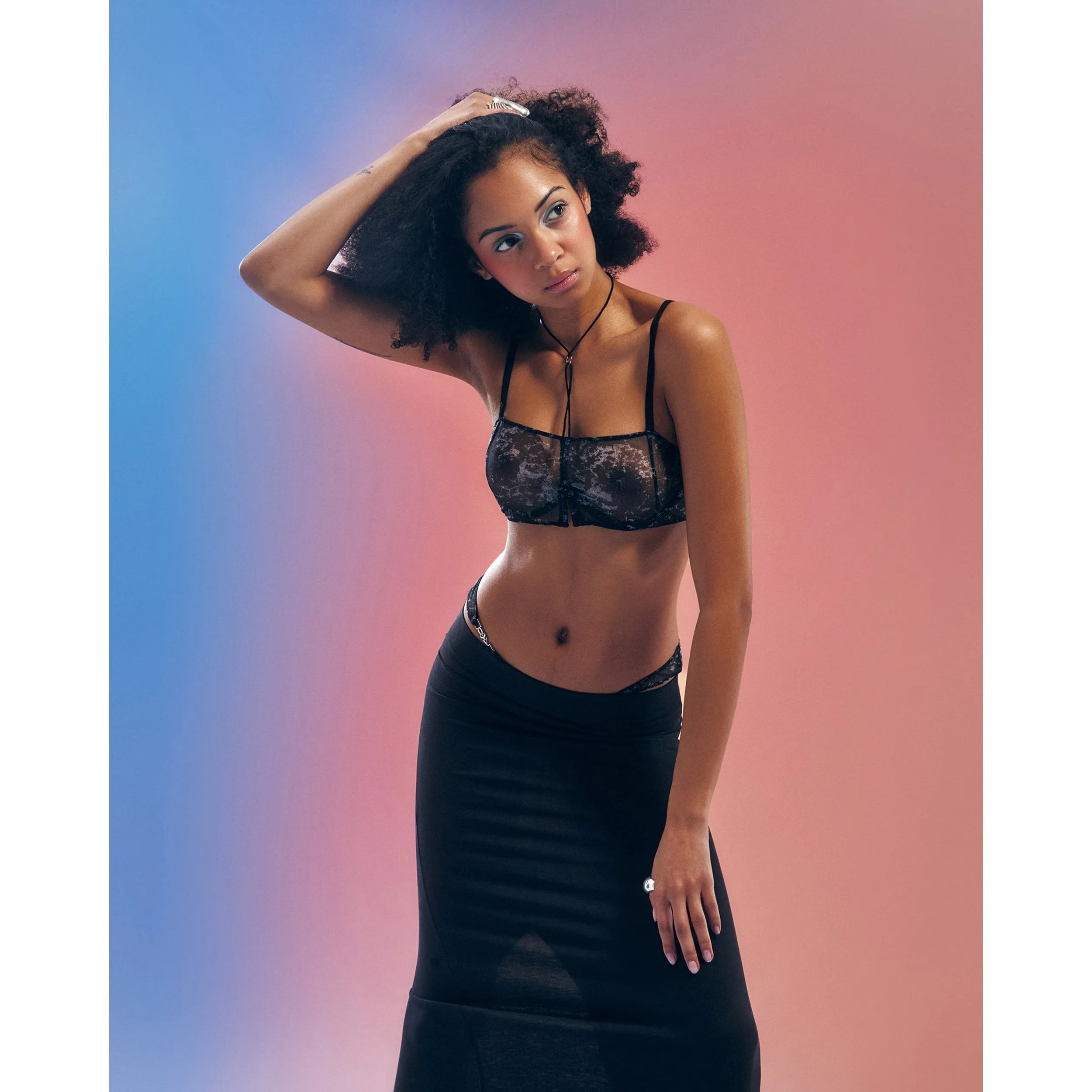 Soutien-gorge Corrosis noir transparent froncé, armatures réglables, motif raffiné, porté par modèle sur fond dégradé.