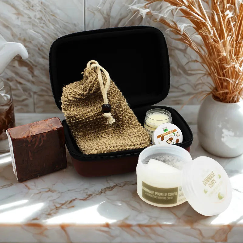 Coffret gommage corps naturel avec pots exfoliants et accessoires dans une trousse noire, sur fond de salle de bain.