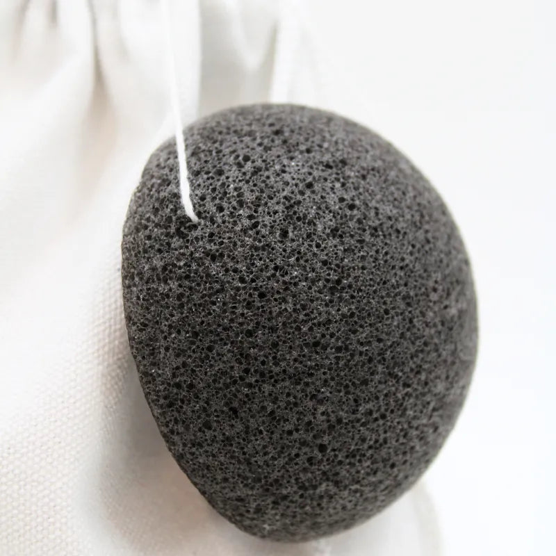 Éponge konjac noire sur fond blanc, accessoire de soin visage pour peau grasse, purifiant et naturel.