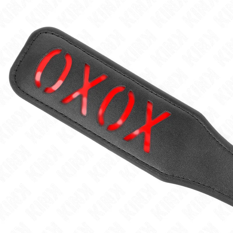 Accessoire BDSM cuir noir premium, pagaie avec motif XOXO découpé, fond rouge, élégant et sophistiqué.