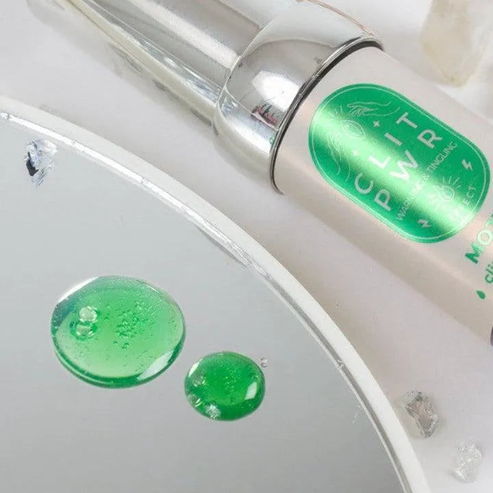Baume clitoridien stimulant effet chaleur, flacon argenté avec étiquette verte, gouttes vertes sur surface réfléchissante.