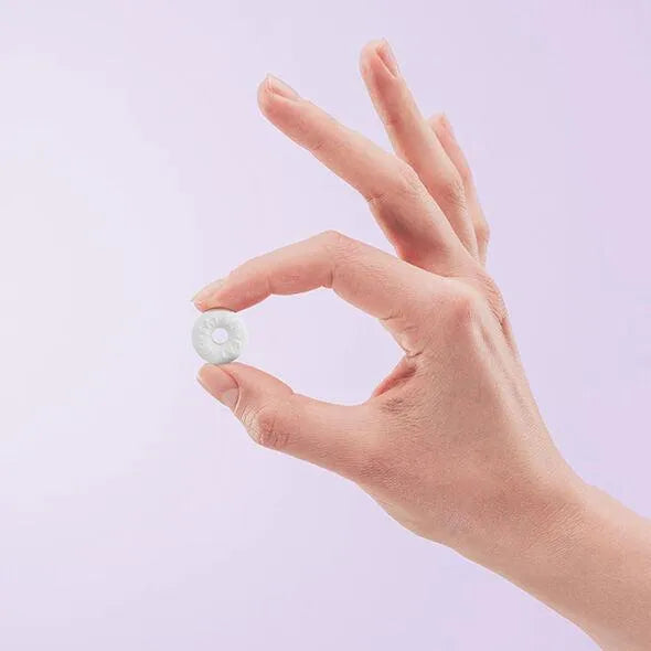 Bonbon mentholé végan sans sucre, blanc, rond, tenu entre deux doigts sur fond violet, pour stimulation sensorielle.
