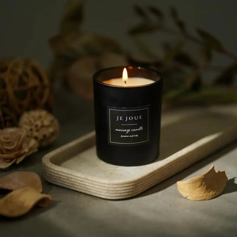 Bougie de massage noire allumée, parfum ylang ylang et mandarine, sur plateau en bois, ambiance relaxante et intime.