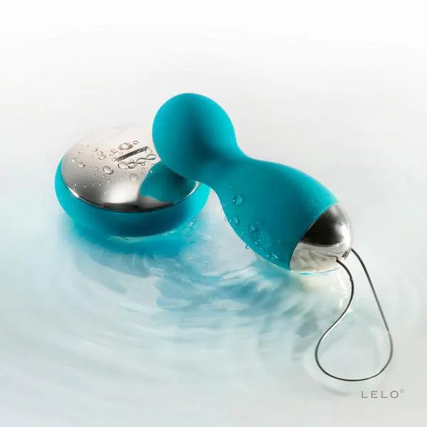 Boules plaisir rotatives vibrantes bleues, silicone, télécommande argentée, submersibles, sur fond d'eau.