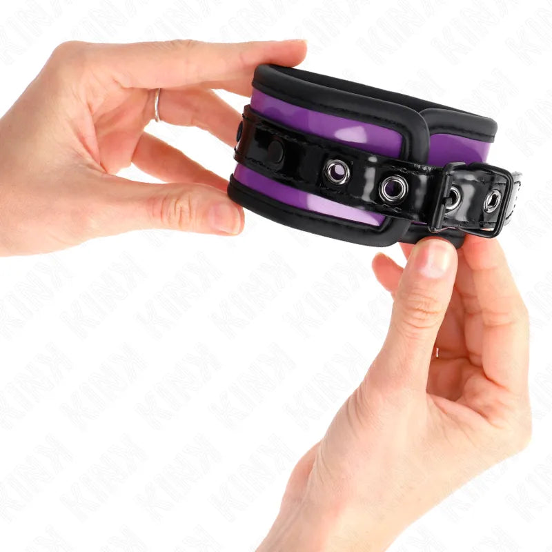 Bracelet BDSM en cuir végétalien violet et noir, ajustable, rembourré, avec boucles métalliques, tenu par des mains.