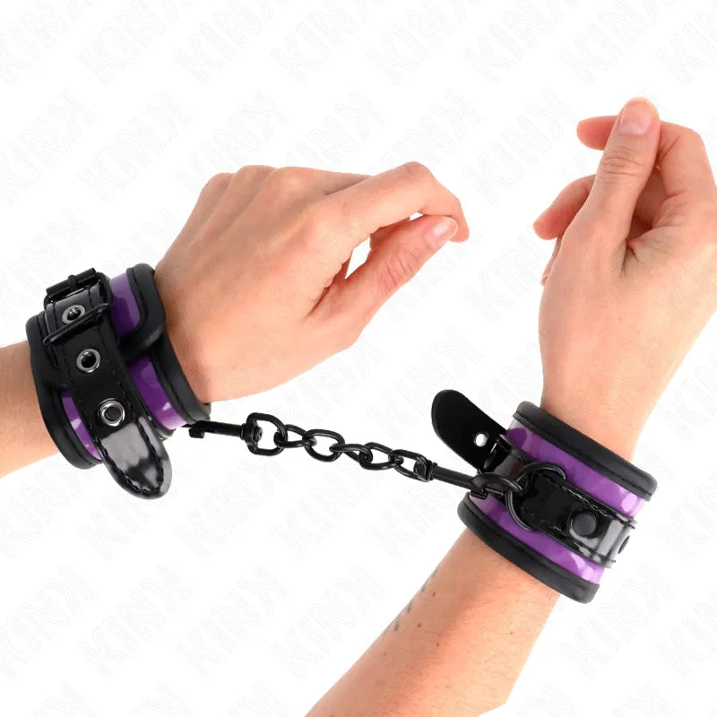 Bracelets BDSM en cuir végétalien violet et noir, ajustables, rembourrés, avec chaîne, portés sur poignets.
