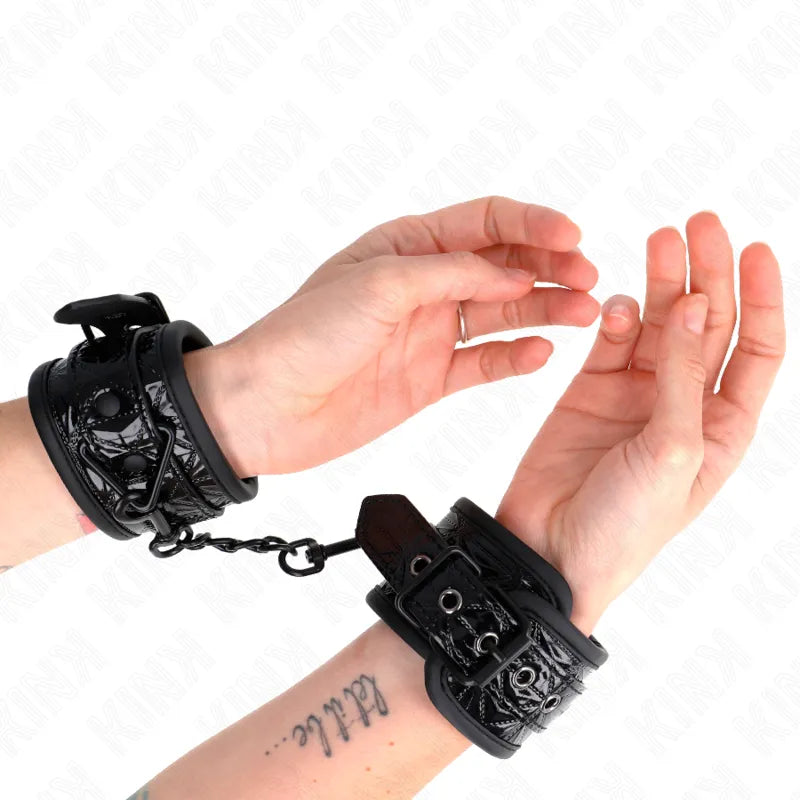 Bracelets BDSM en cuir noir véritable, rembourrés, avec fermetures réglables et anneaux robustes, portés sur poignets.