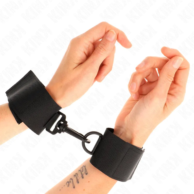 Bracelets en cuir noir BDSM avec rembourrage, boucles métalliques et velcro, portés sur poignets, anneau de fixation central.