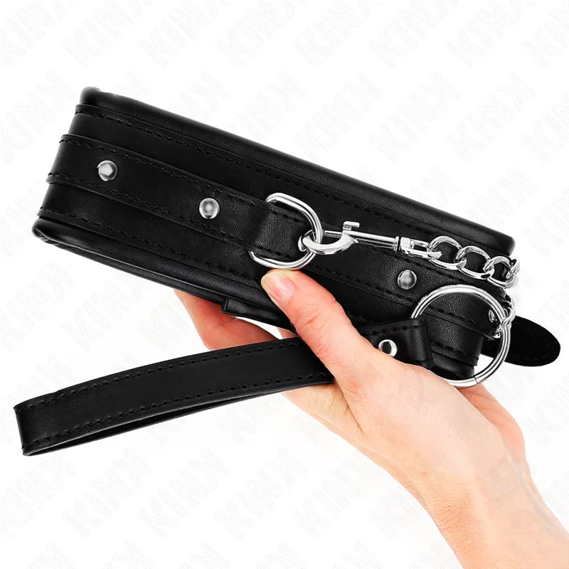Collier BDSM en cuir noir avec boucles métalliques polies, design élégant et robuste, tenu dans une main.