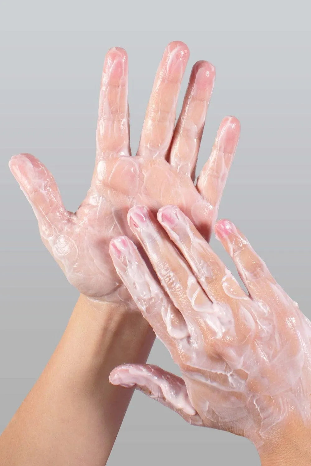 Crème raffermissante blanche sur mains, texture lisse, enrichie en extraits naturels pour peaux sensibles, fond gris.