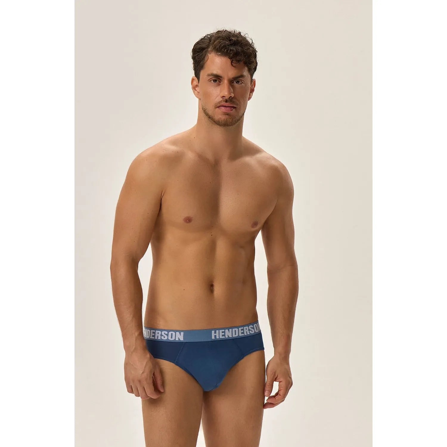 Homme portant slip Henderson bleu foncé, coupe classique, ceinture élastique large avec logo contrastant, fond neutre.