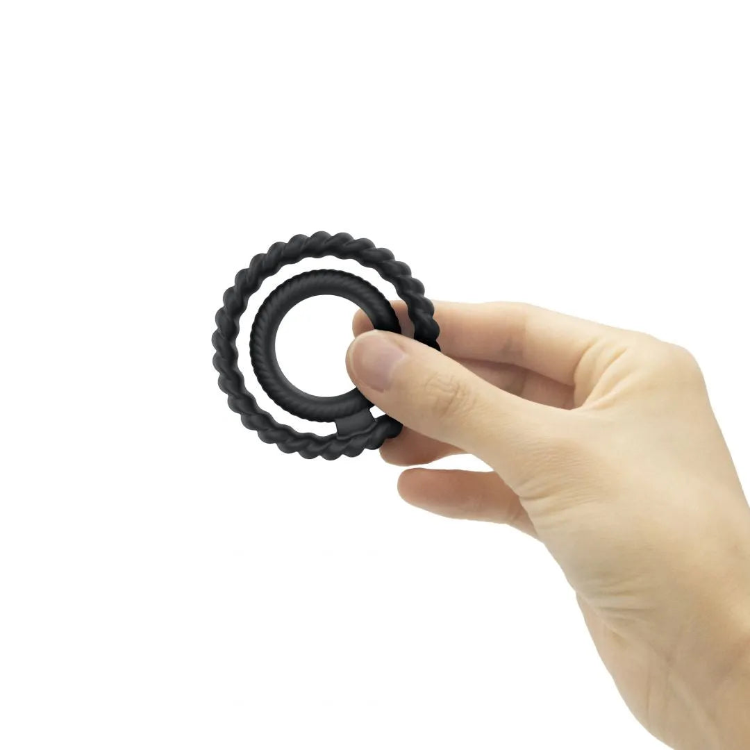 Anneau silicone noir double stimulation, cannelé, flexible, étanche, pour érections longues, tenu par une main.