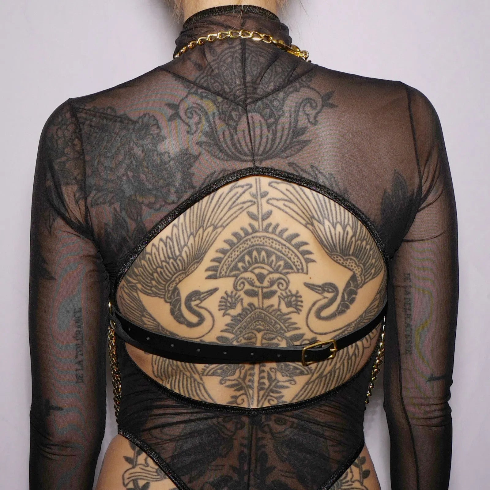 Harnais poitrine cuir noir avec chaînes argentées, ajustable, élégant, porté sur un haut transparent, style audacieux.