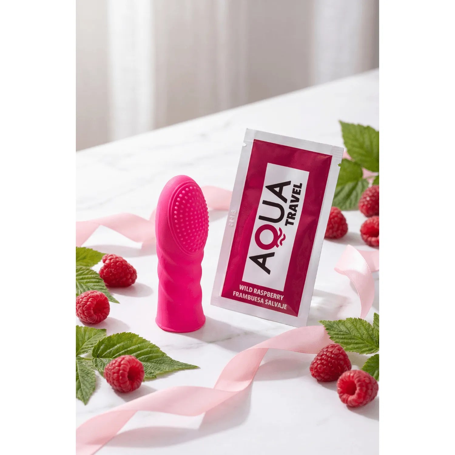 Doigt Chinois rose en silicone texturé, ergonomique, avec picots, posé sur une table avec framboises et sachet Aqua Travel.