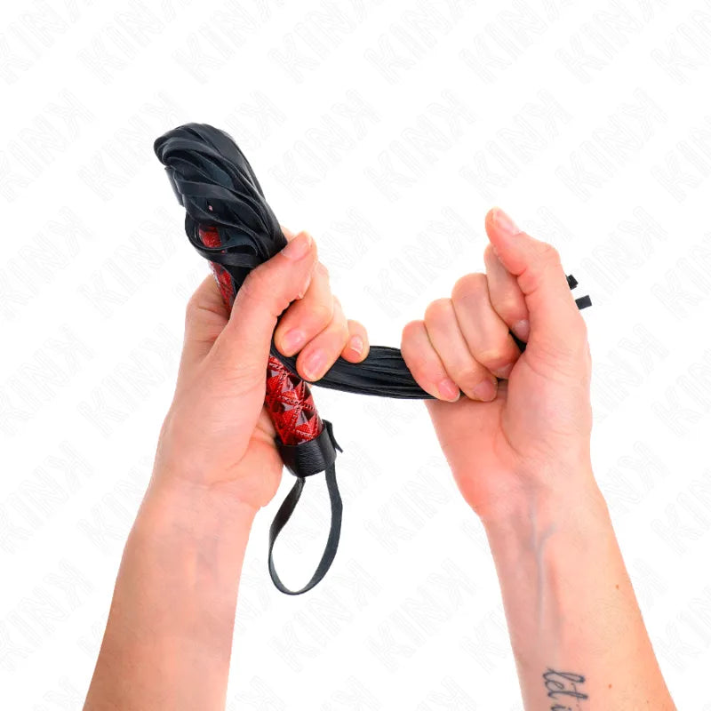 Accessoire BDSM en cuir rouge et noir, cravache élégante tenue par deux mains, qualité premium, plaisir raffiné.