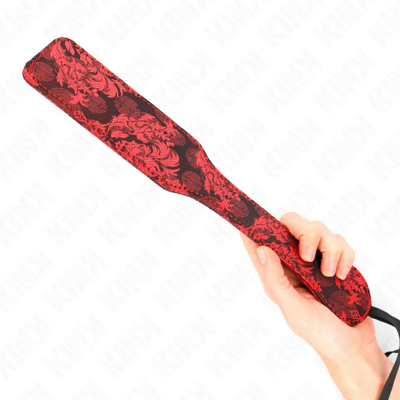Pagaie BDSM en cuir rouge et noir, motifs élégants, tenue en main, accessoire artisanal de luxe pour expériences intimes.