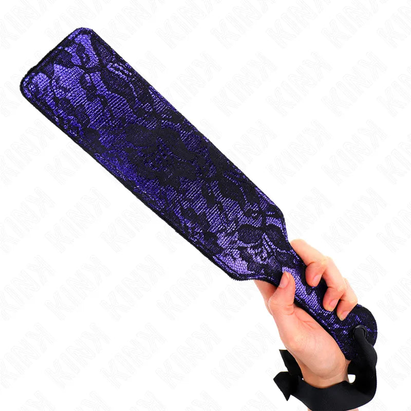 Pagaie BDSM luxe en cuir violet et noir, motif dentelle, tenue en main, élégance et sensualité.
