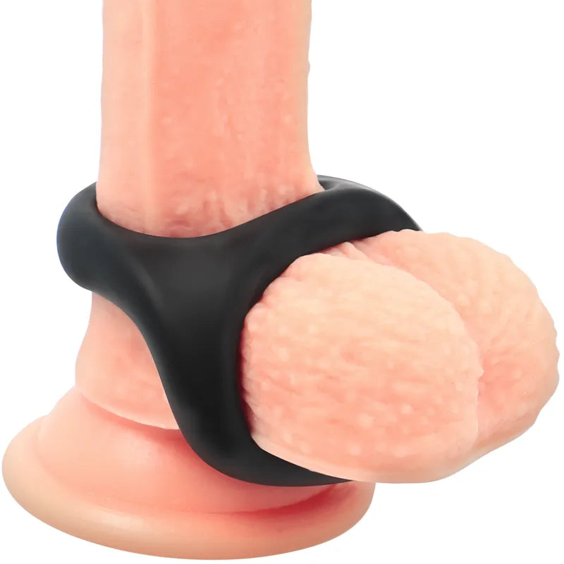 Anneau pénien noir en silicone hypoallergénique, extensible, avec maintien scrotum intégré, sur fond neutre.