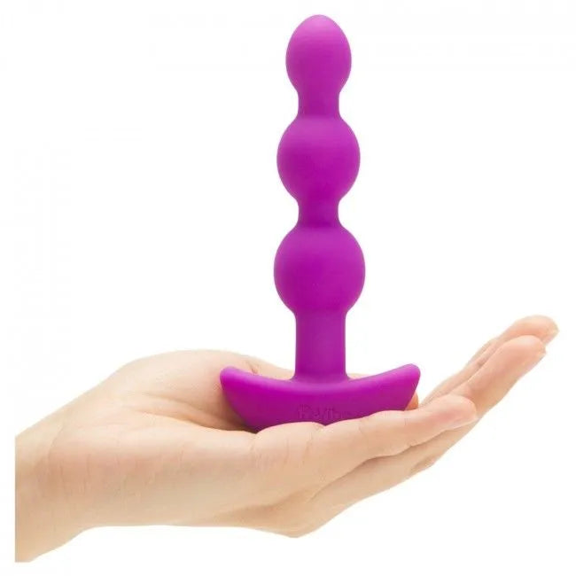 Plug anal violet en silicone avec trois perles, tenu dans une main, conçu pour vibrations puissantes et confort optimal.