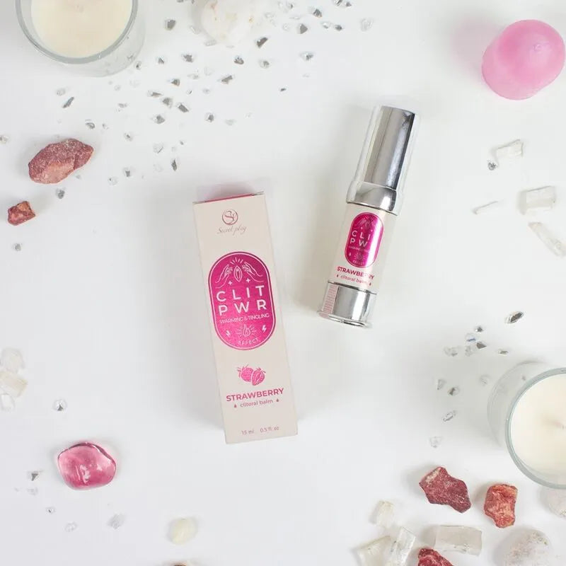 Baume chauffant clitoridien fraise 15ml, flacon argenté et boîte rose, sur fond décoratif avec pierres et bougies.