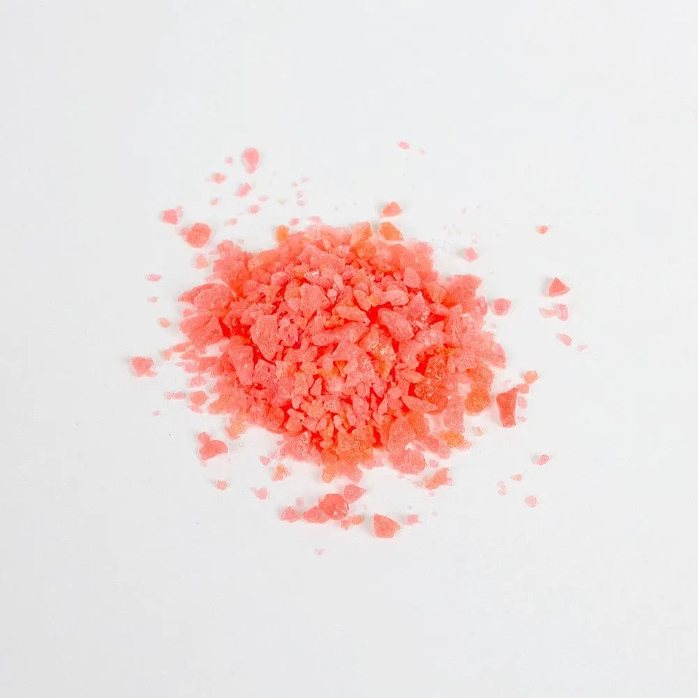 Bonbons pétillants roses pastèque pour moments intimes, texture granuleuse, sur fond blanc, sachet 9g.