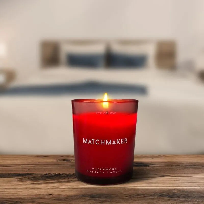 Bougie de massage rouge allumée sur table en bois, ambiance chaleureuse, ingrédients naturels, parfum cèdre et cassis.