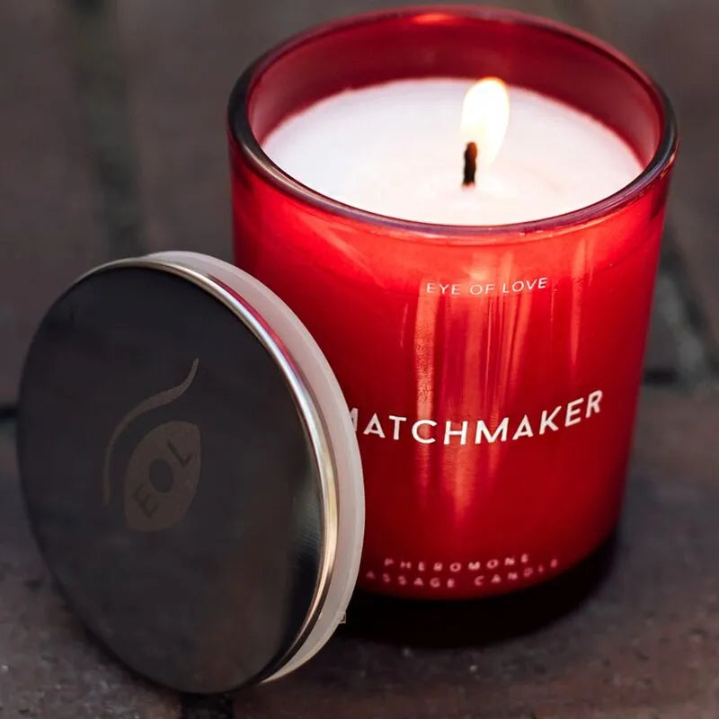 Bougie de massage phéromones rouge allumée, couvercle noir, parfum cèdre, cassis, citron, éthique et végétalienne.