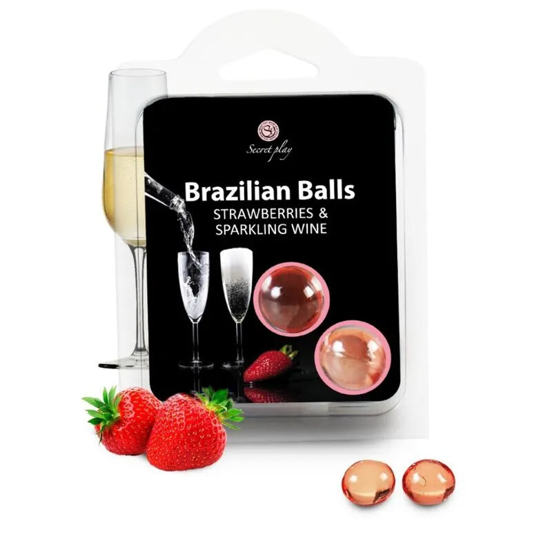 Boules huile massage fraise champagne, rouges et translucides, fondantes, avec fraises et verre de champagne en arrière-plan.