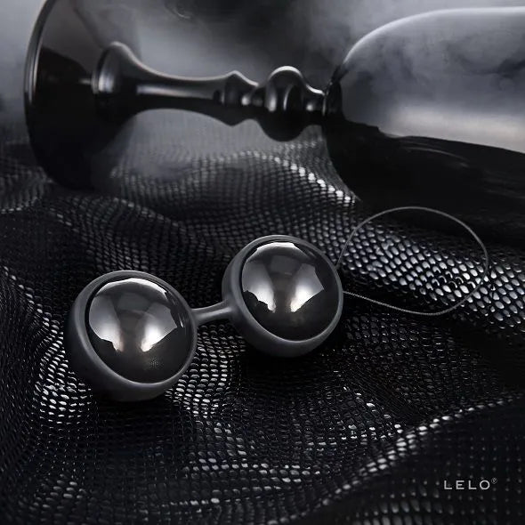 Boules de Kegel noires en silicone, élégantes et ergonomiques, sur fond texturé avec pochette satinée et cordon hygiénique.