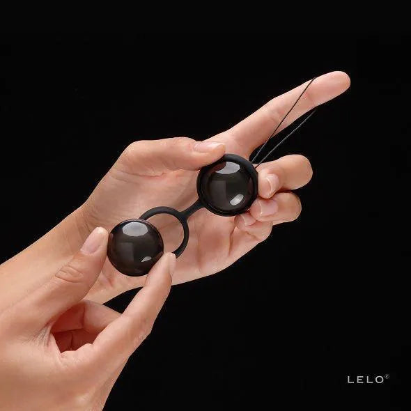 Boules de Kegel noires en silicone, ergonomiques, tenues en main, avec cordon hygiénique, sur fond noir.