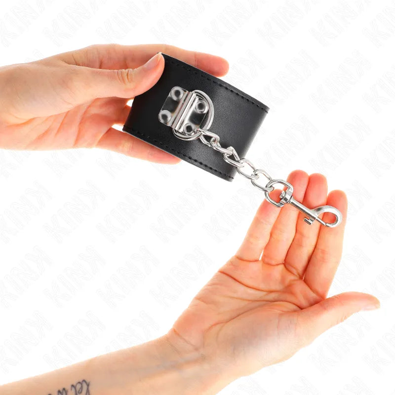 Bracelet BDSM en cuir noir avec fermetures en métal robuste, design épuré et ergonomique, tenu par deux mains.