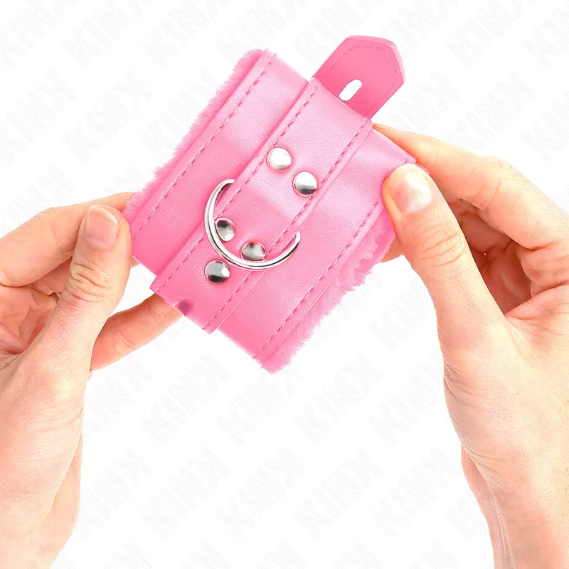 Bracelet BDSM rose en cuir végétalien, rembourré, avec anneau métallique et finitions personnalisables, tenu en main.