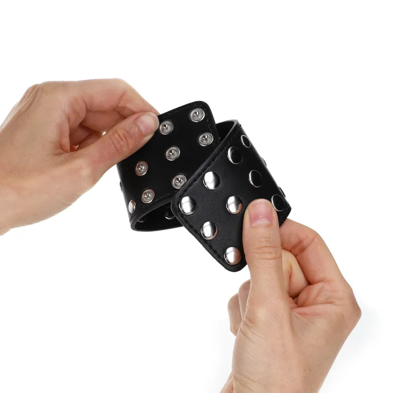 Bracelet BDSM noir en cuir végétalien avec rivets métalliques, élégant et ajustable, tenu par deux mains.