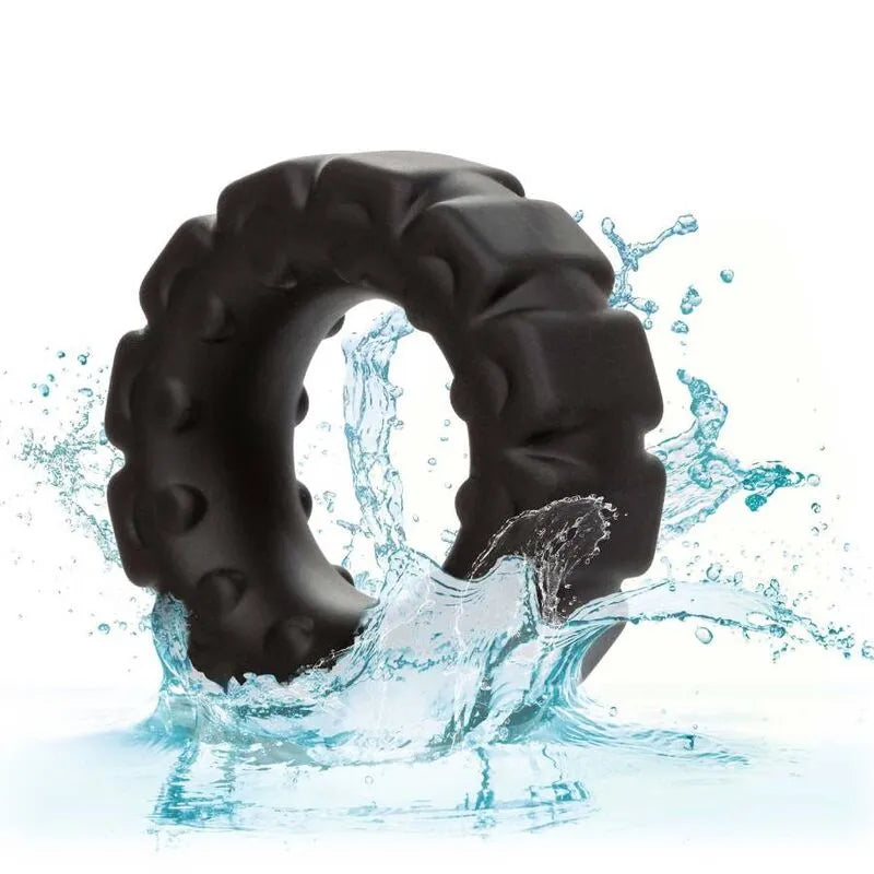 Anneau pénien noir en silicone liquide, texturé, étanche, élastique, sur fond blanc avec éclaboussures d'eau.
