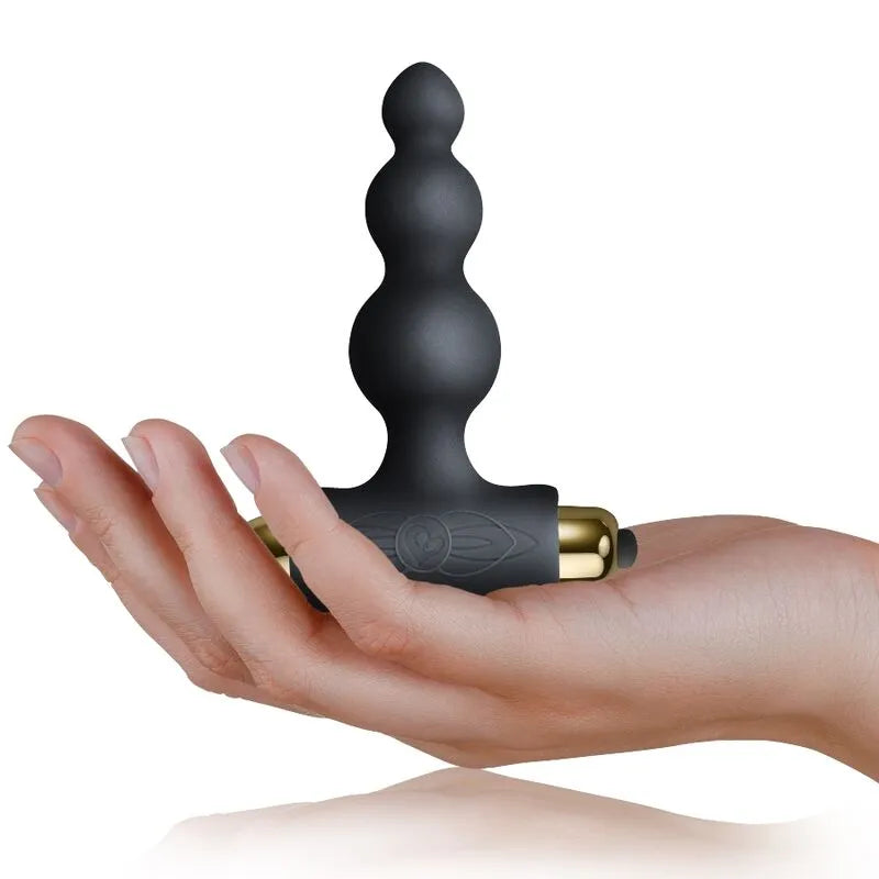 Anneau vibrant noir en silicone doux, forme ergonomique, avec module vibrant doré, tenu dans une main.