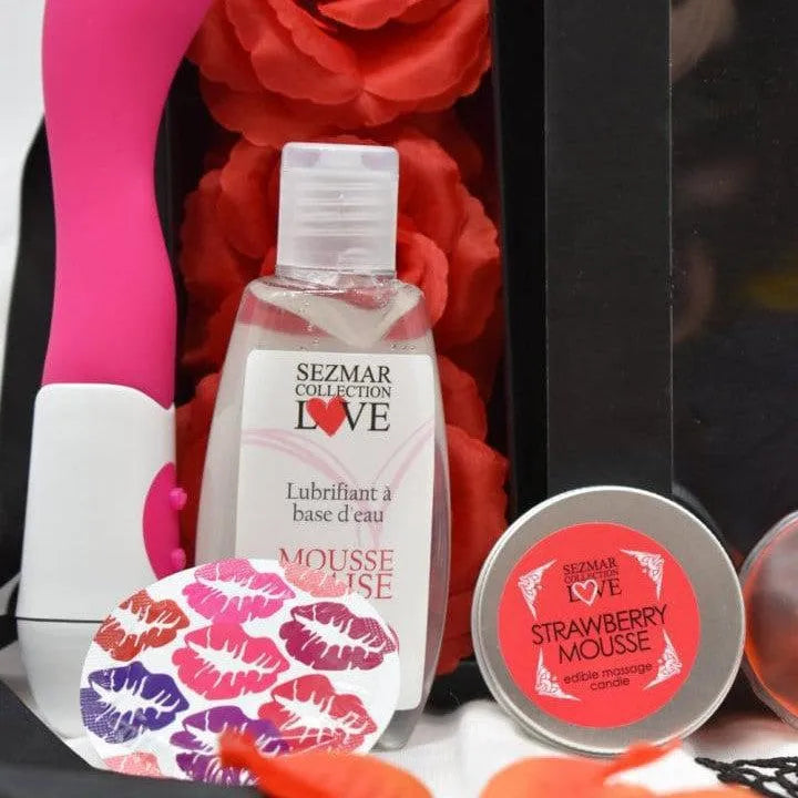Coffret coquin édition limitée avec accessoires intimes colorés, lubrifiant, mousse fraise, et pétales rouges.