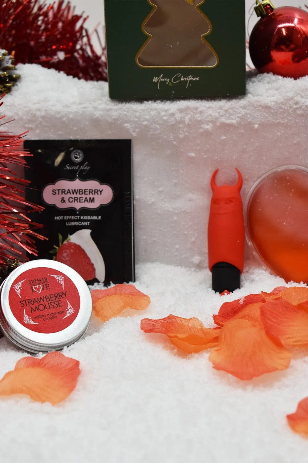 Coffret massage Noël: huile fraise, cœur chauffant, bougie, pétales de rose, mini vibromasseur rouge sur fond festif.