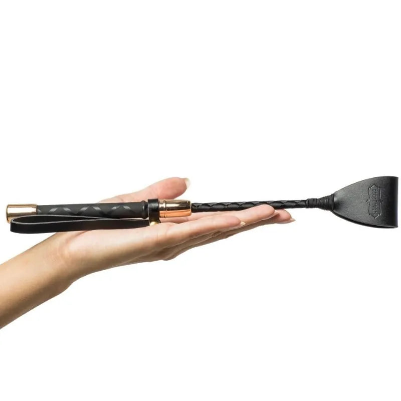 Cravache élégante noire avec détails dorés, accessoire du coffret érotique Kamasutra édition limitée, tenue en main.