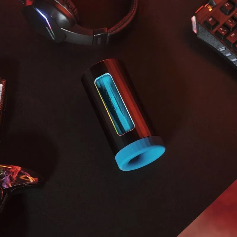 Console de plaisir silicone noire et bleue, forme cylindrique, sur bureau avec accessoires gaming, connectée et interactive.