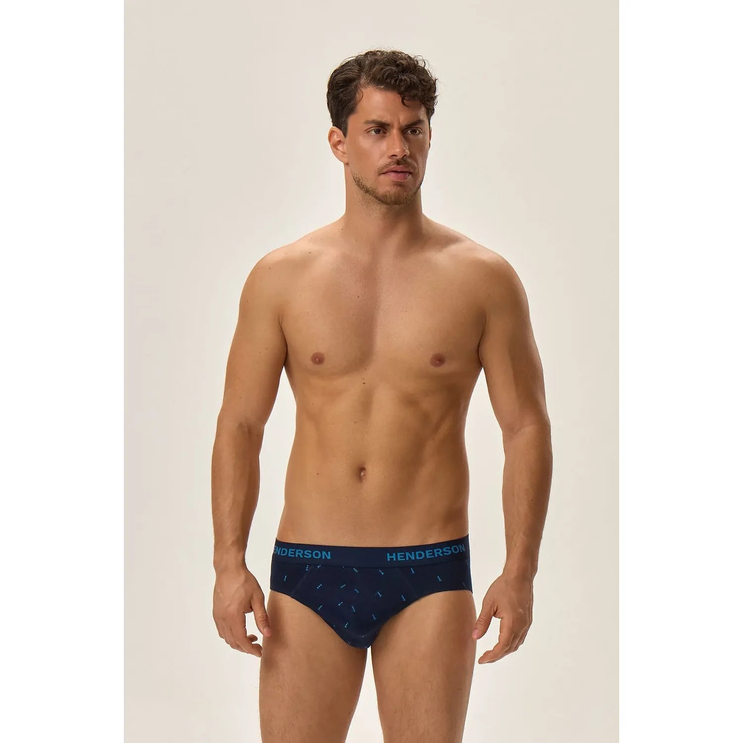 Homme portant slip bleu marine imprimé marin, ceinture élastique, coupe ajustée, confort coton élasthanne, fond beige.