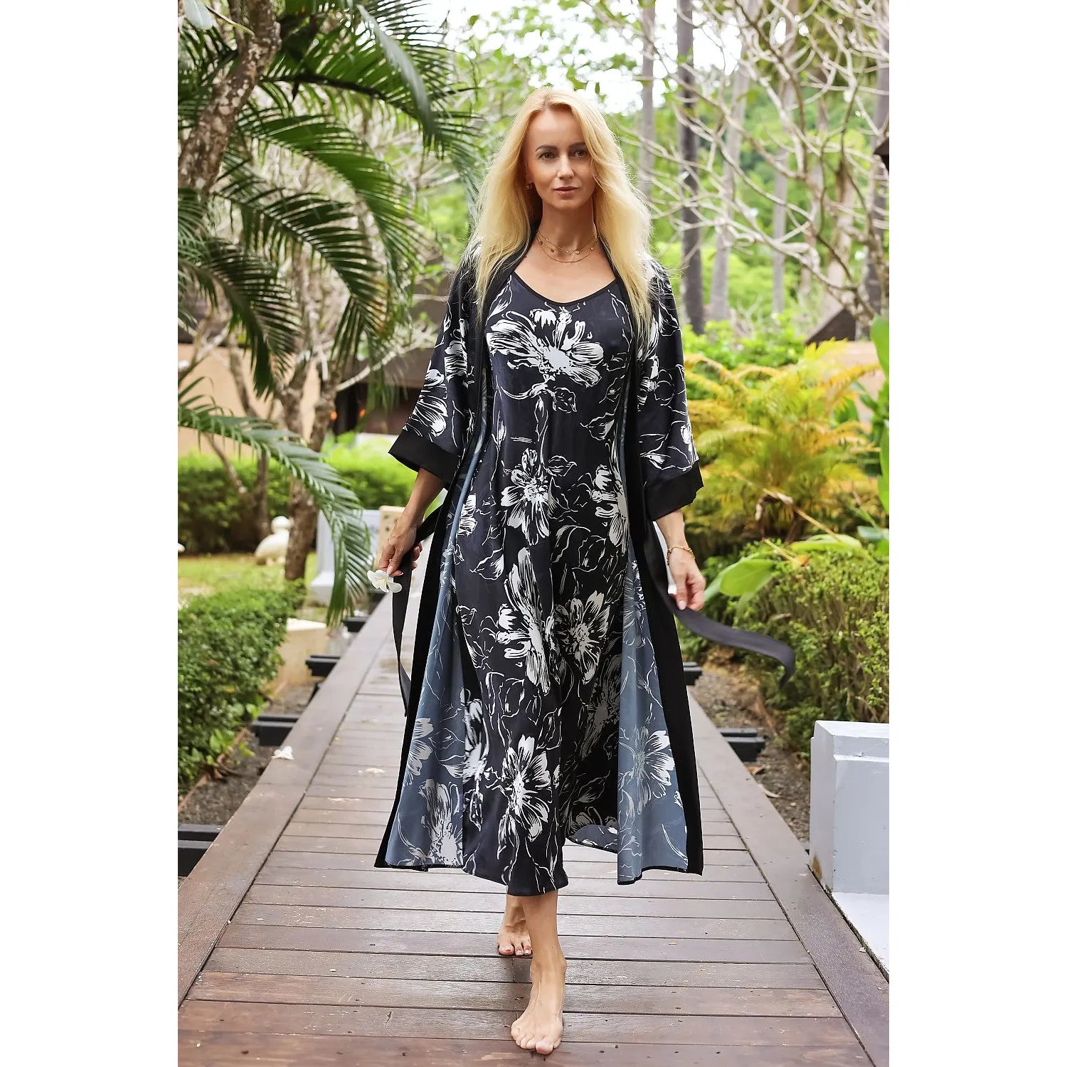 Chemise de nuit longue en satin soyeux Kalimo, motif exotique floral, élégante et raffinée, fond noir, femme en extérieur.