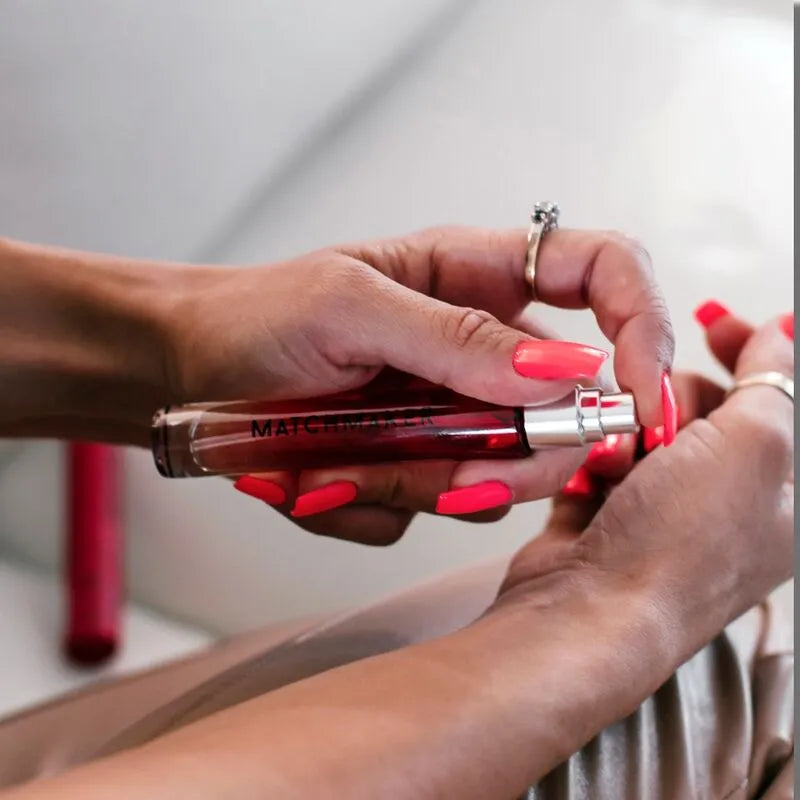 Flacon de cologne en verre transparent, format voyage, avec vaporisateur, tenu par une main aux ongles vernis rouge.