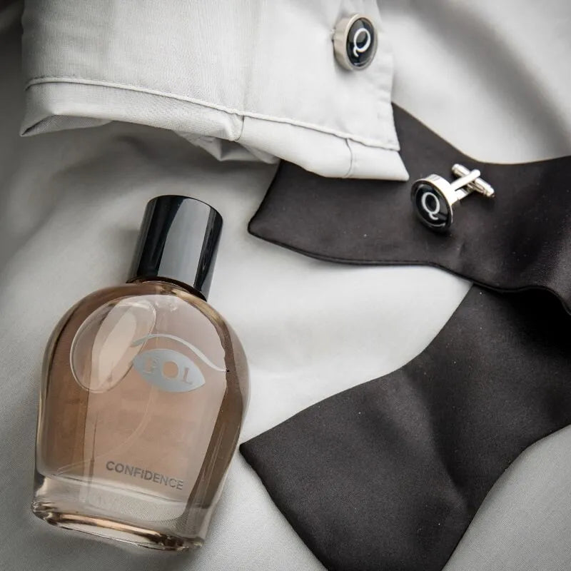 Flacon de cologne phéromone pour homme, design élégant, bouchon noir, posé sur chemise blanche et nœud papillon noir.