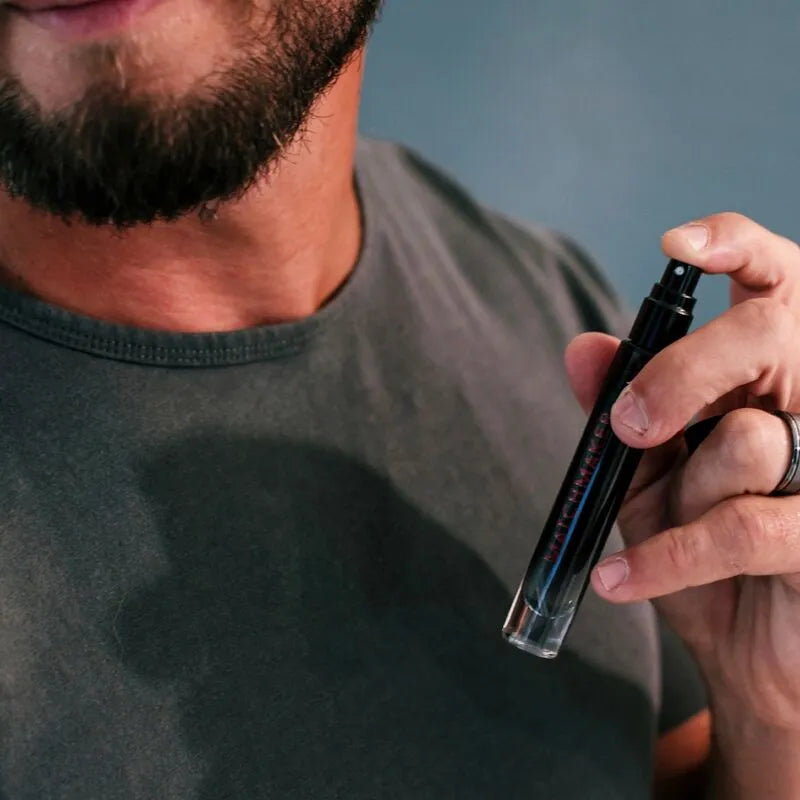 Flacon vaporisateur noir élégant de cologne phéromones cèdre cassis citron, tenu par un homme, fond neutre.