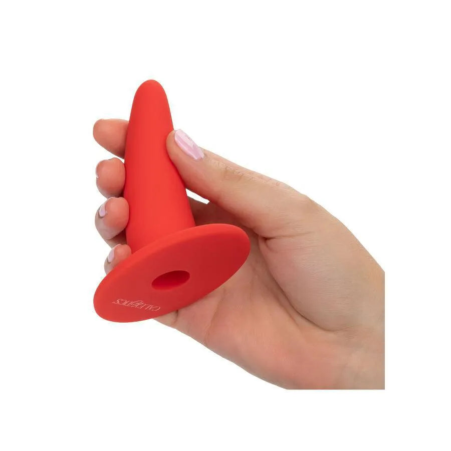 Dilatateur vaginal rouge en silicone hypoallergénique, forme ergonomique, base incurvée, tenu dans une main.