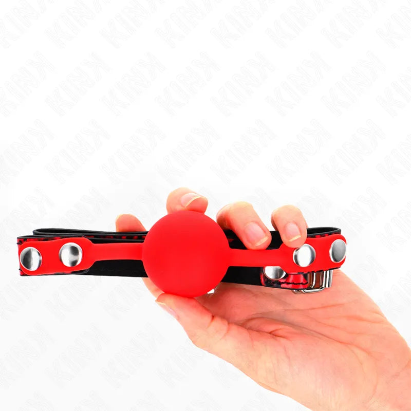 Gag BDSM rouge en silicone doux avec sangle noire ajustable et boucles métalliques, tenu dans une main.