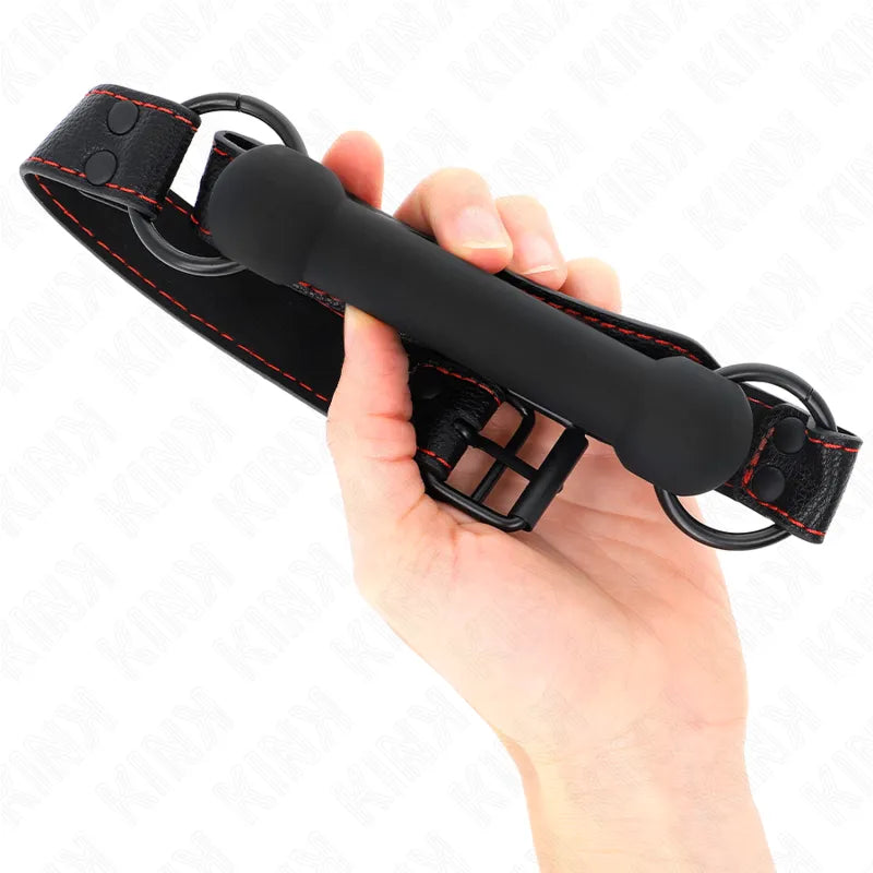 Gag BDSM en silicone noir avec bretelles réglables en cuir noir et surpiqûres rouges, tenu dans une main.