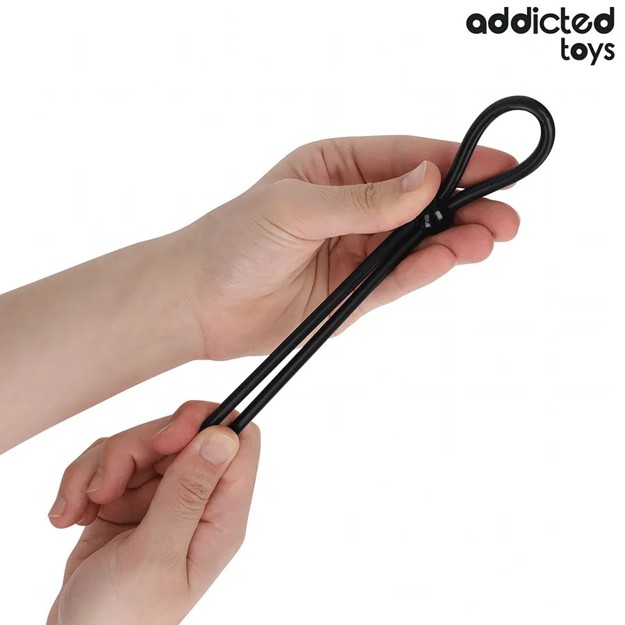 Corde pénis silicone noire boucle unique, flexible et réglable, pour stimulation et érection, tenue par des mains.